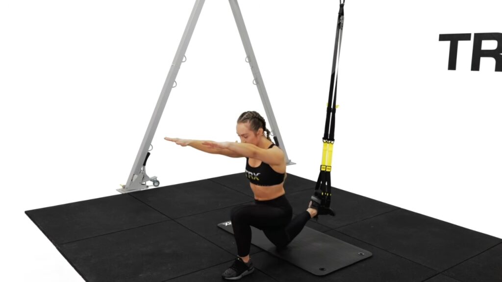 Woman performs a supported split squat with TRX suspension straps.