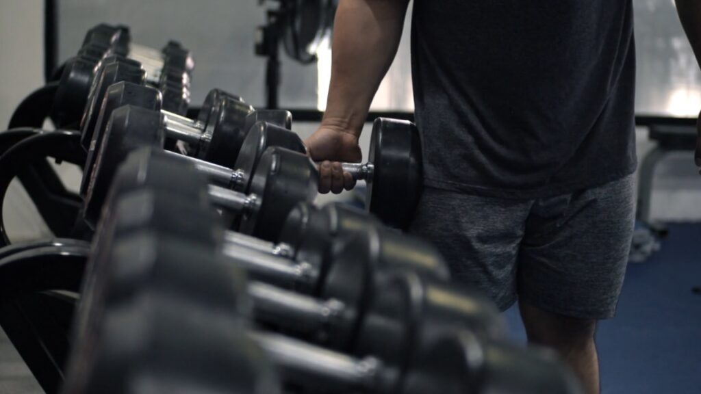 A man holds a dumbbell beside a rack of weights at the gym.