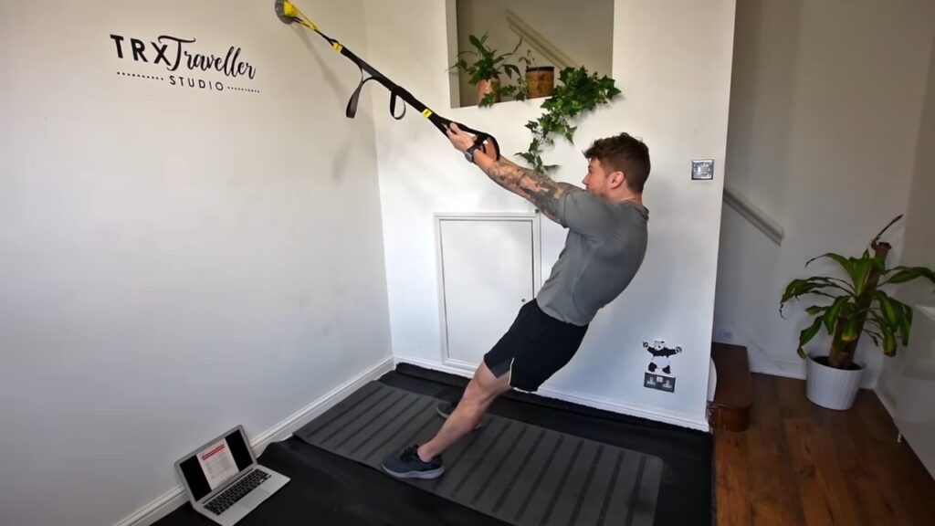 Man performs a TRX row with suspension straps anchored to a wall.