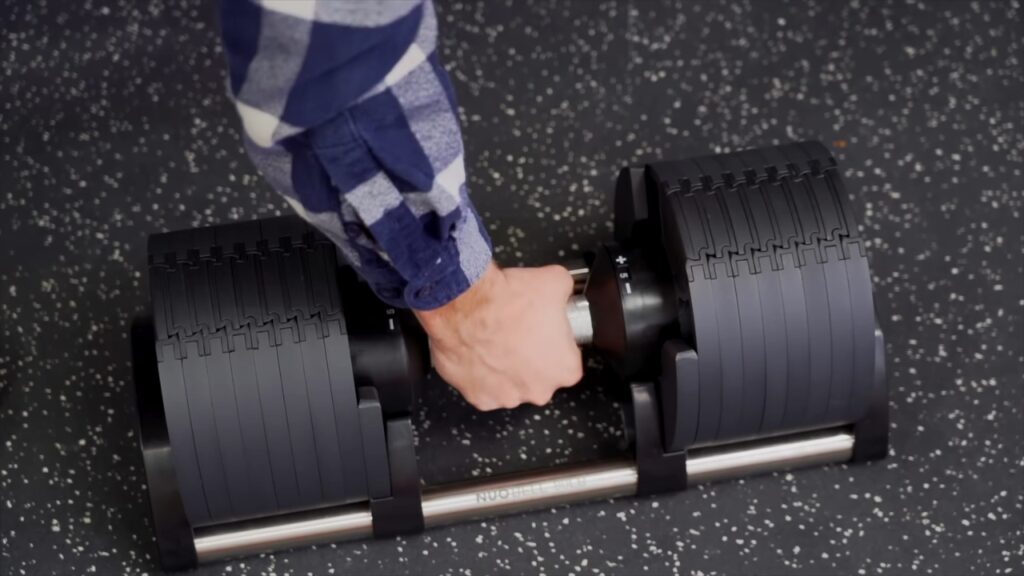 A hand lifts an adjustable dumbbell in a garage gym.
