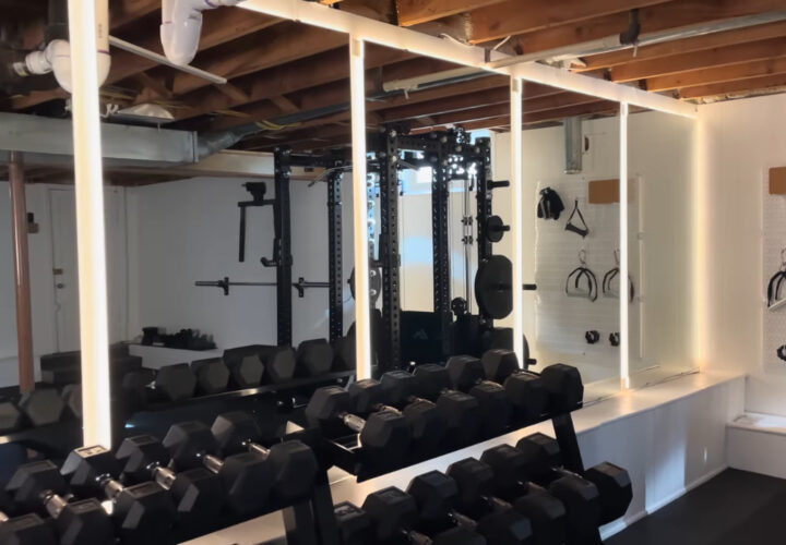 Basement gym with dumbbell racks, wall mirrors, LED lights, and exposed ceiling beams.