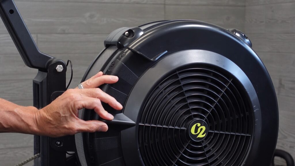 A hand adjusts the damper lever on a Concept2 rowing machine flywheel.
