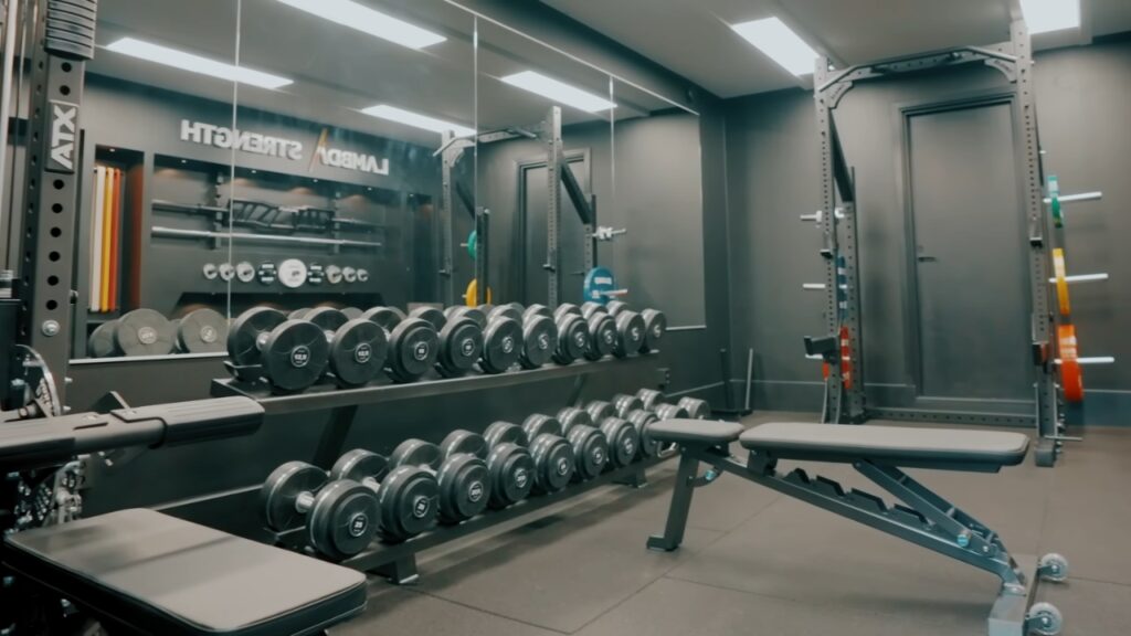 A compact gym with rows of dumbbells, adjustable weight benches and a squat rack.