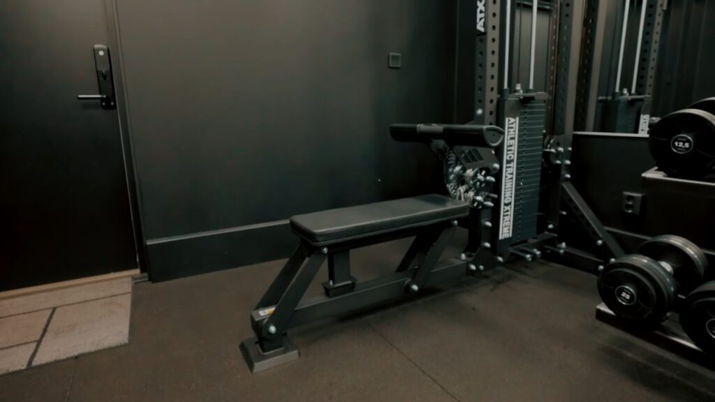 A home gym with a weight bench, cable machine and dumbbell rack on rubber flooring.
