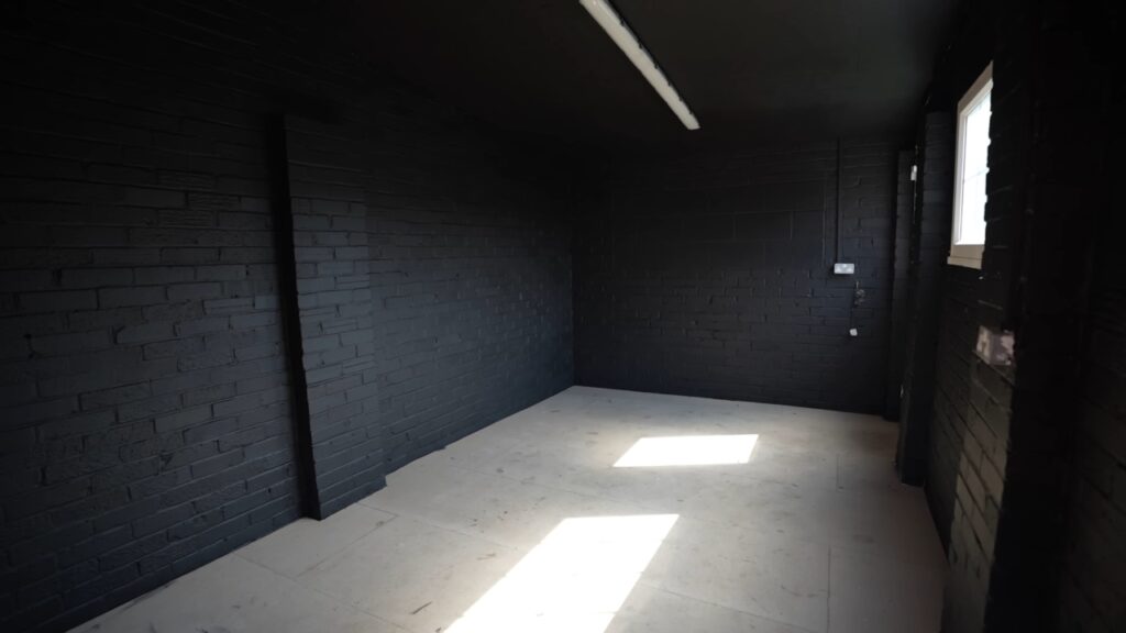 An empty room with black brick walls and a concrete floor ready for a home gym.
