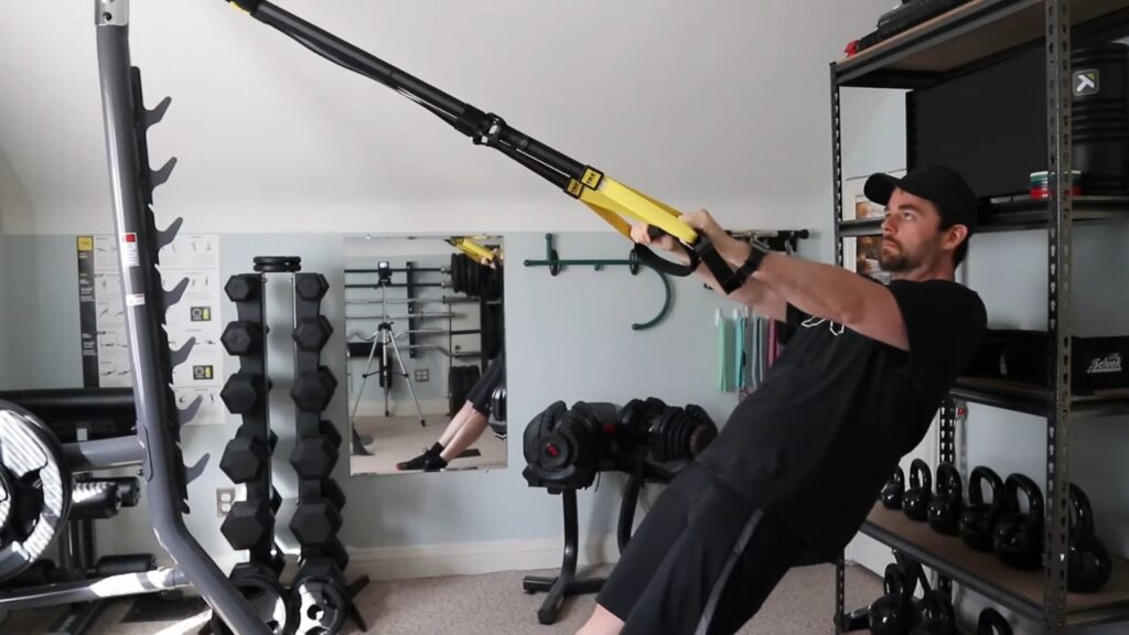 A man uses a suspension trainer in a small garage gym.