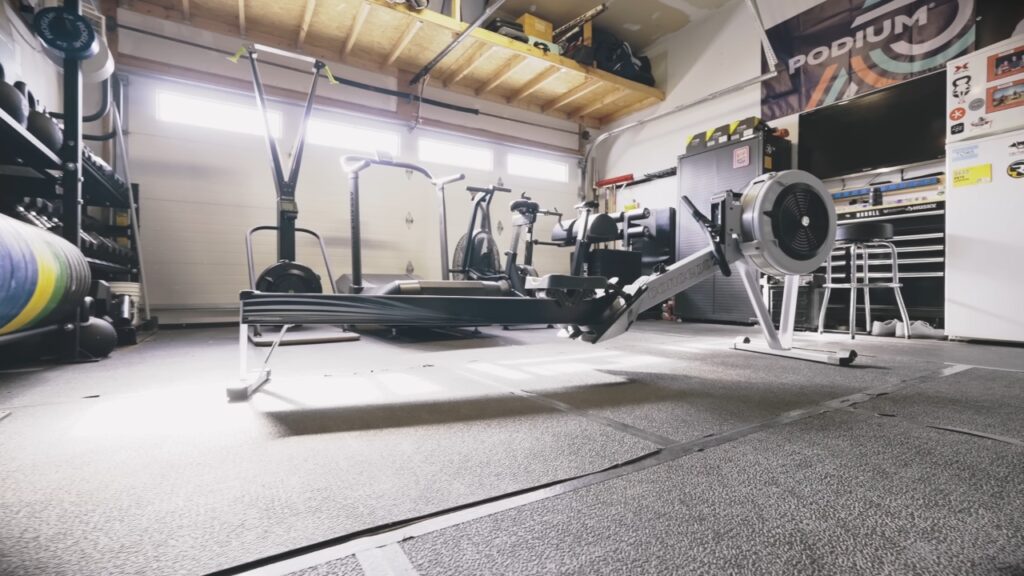 A rowing machine and strength equipment fill a two-person garage gym.