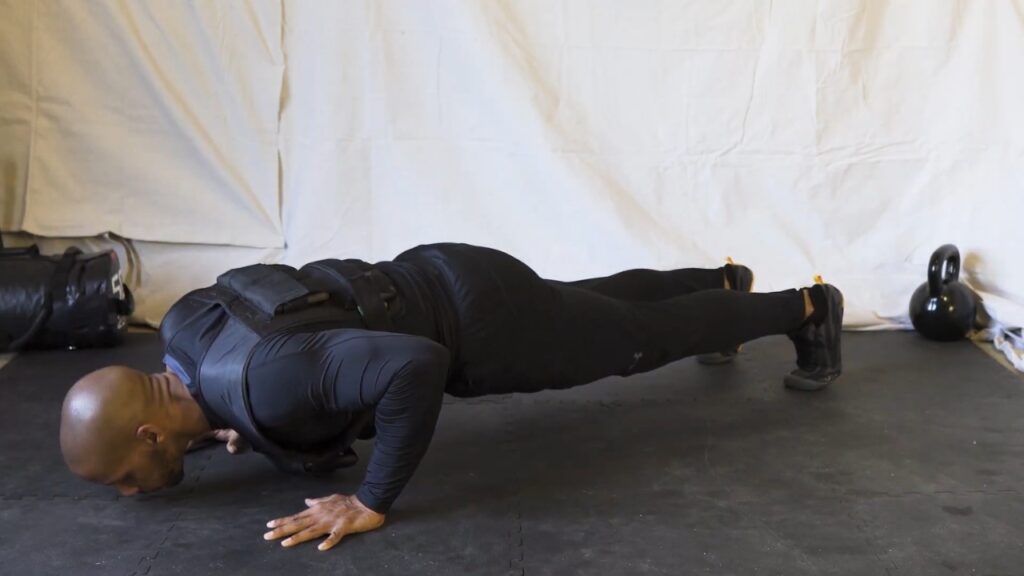 A man does push-ups with a weighted vest on a garage floor.